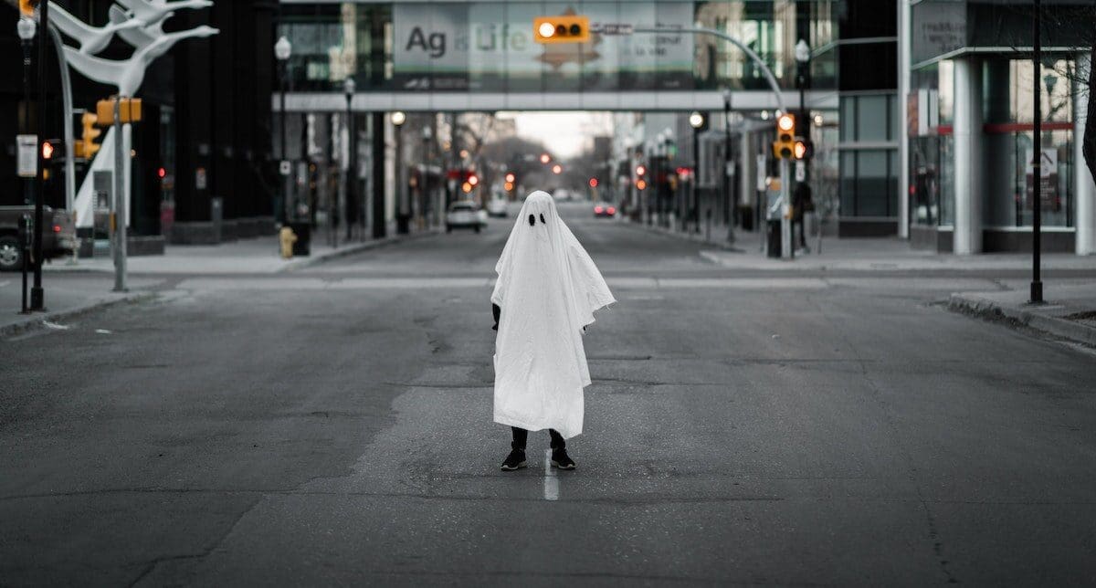 Person standing in the street covered in a white sheet resembling a ghost costume Person standing in the street covered in a white sheet resembling a ghost costume