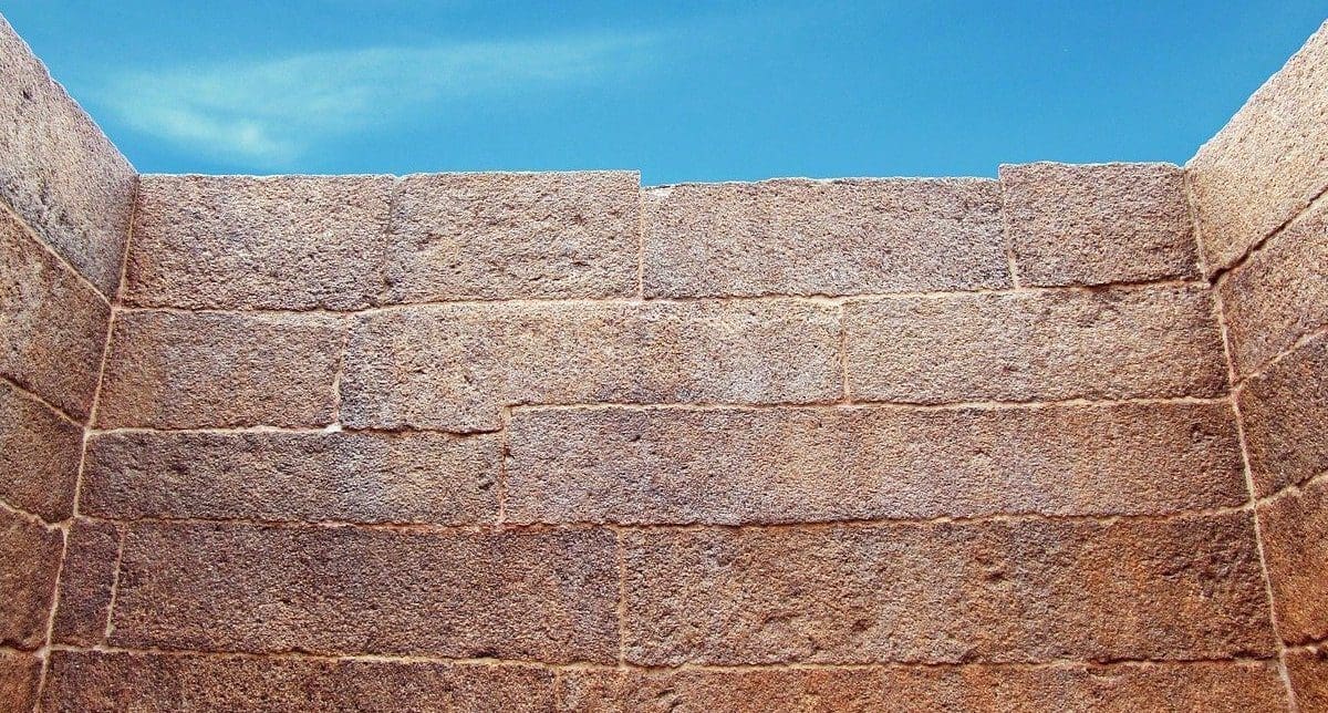 A tall brick wall obscuring most of the view of blue skies
